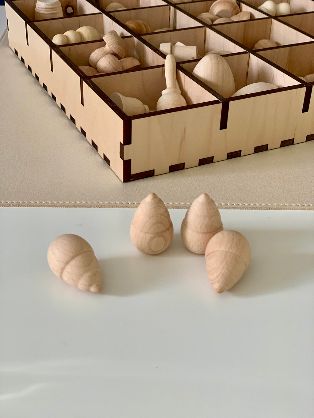 Four smooth natural wooden cone shapes arranged on a light surface with a wooden storage box in the background
