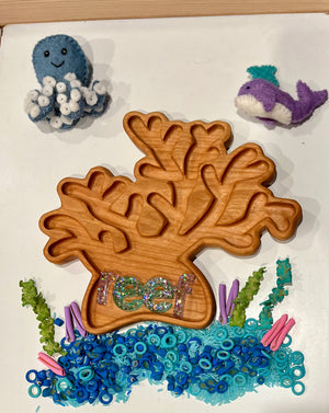Wooden coral-shaped tray on white surface surrounded by felt sea creatures and blue and green small beads