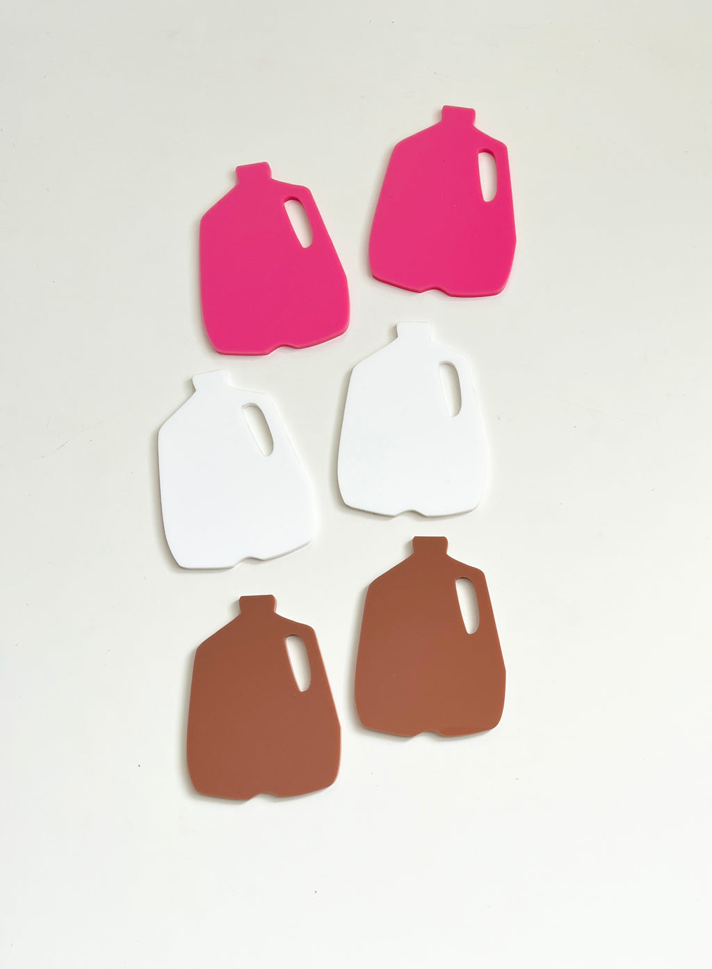 Six plastic jug-shaped cutouts in pink, white, and brown colors arranged on a white surface