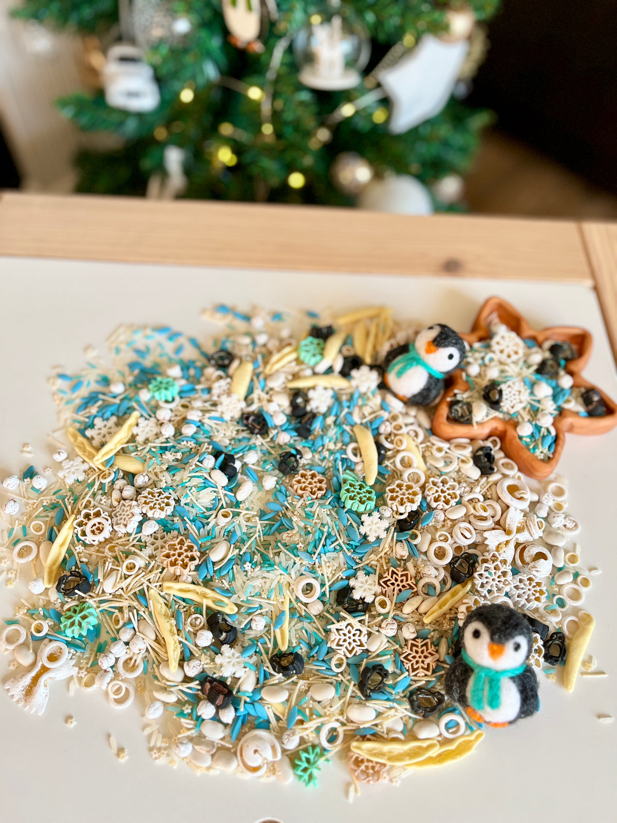 Winter-themed sensory materials including blue, white, and beige dried botanicals with two small felt penguins on white surface
