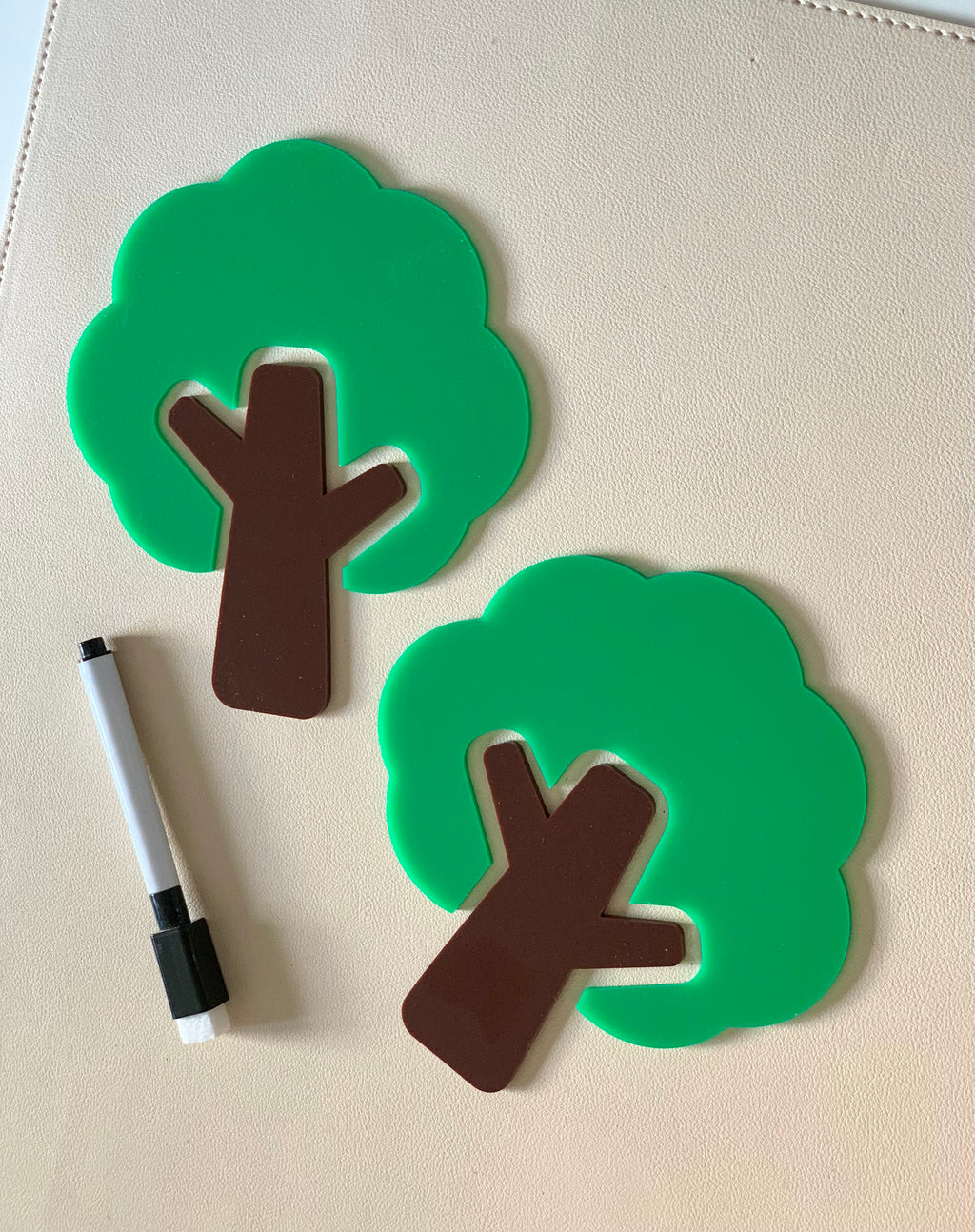 Two green and brown tree-shaped dry erase boards with a black and white marker on a beige surface