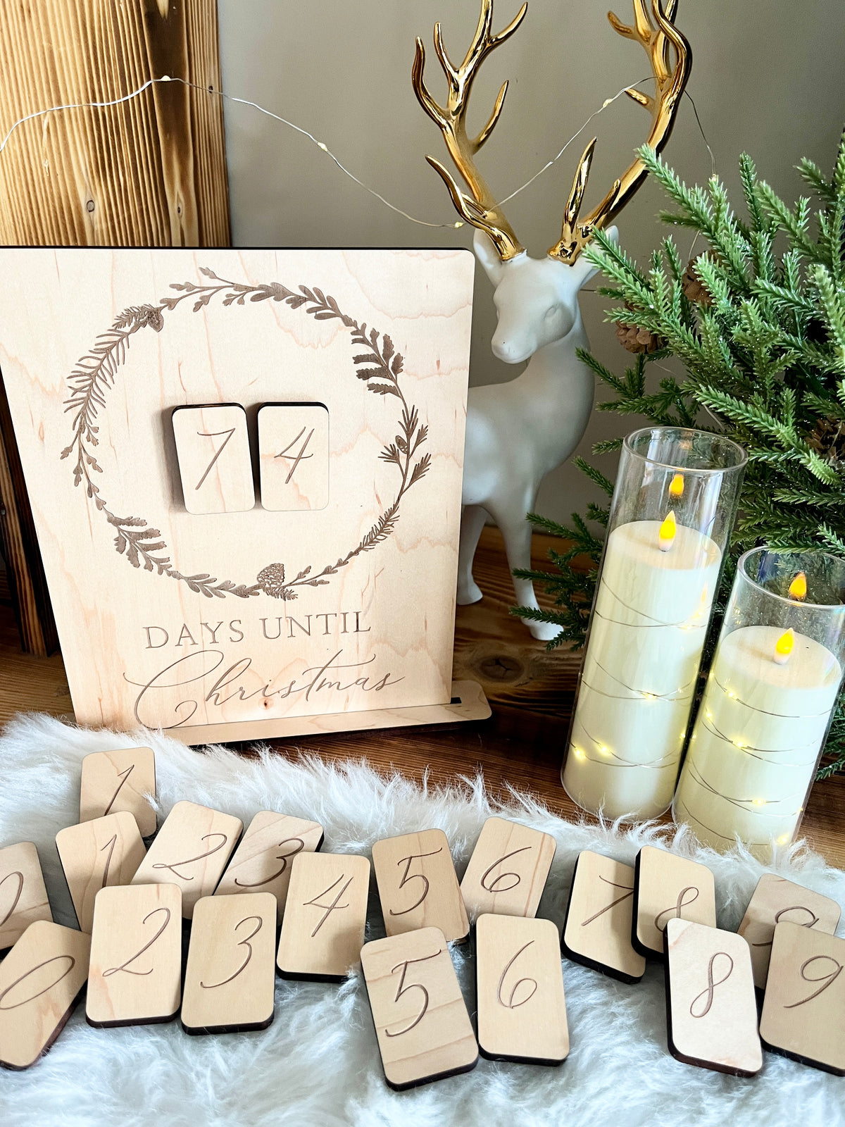 Wooden countdown calendar with interchangeable number tiles, golden antler deer figurine, and glowing LED candles on wood surface