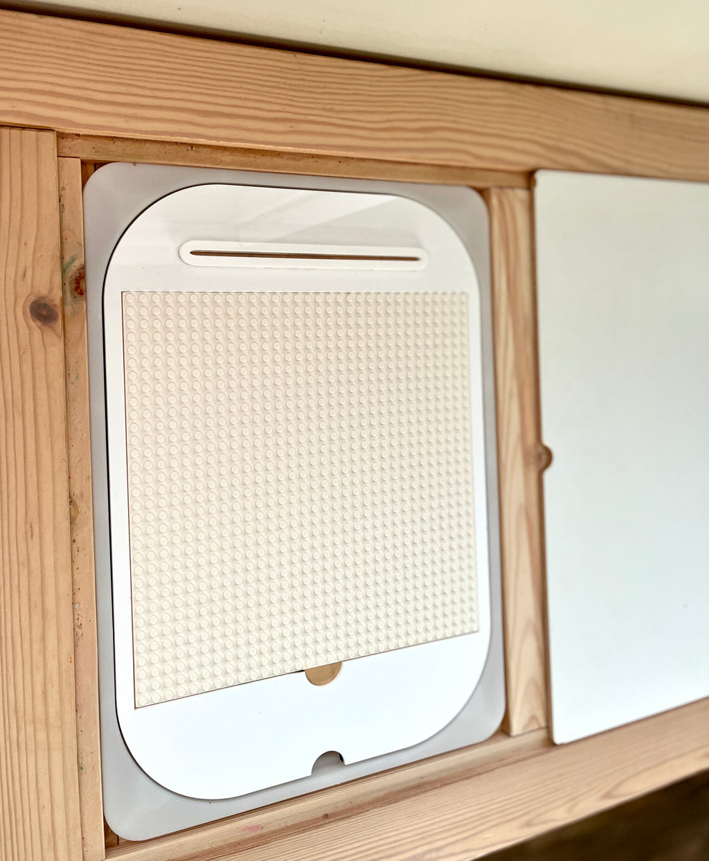 White plastic board with small round studs set inside a wooden frame on a light-colored surface