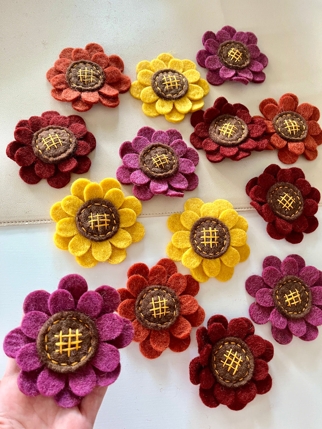 Assorted felt flowers in yellow, purple, red, and orange with stitched brown centers on a light surface