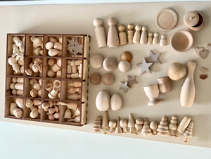 Variety of smooth natural unfinished wooden shapes including peg dolls, stars, trees, bowls, and spheres on light surface