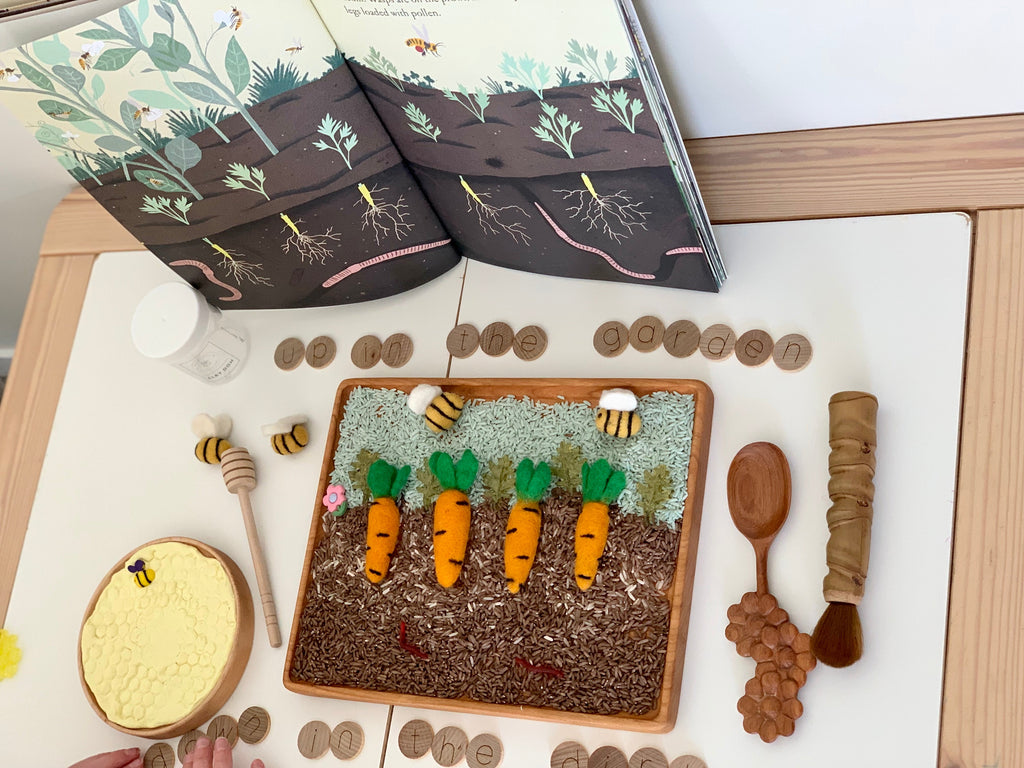 Large rectangular writing tray with felt carrots, wooden bees, honeycomb toy, wooden tokens, and open nature book on table
