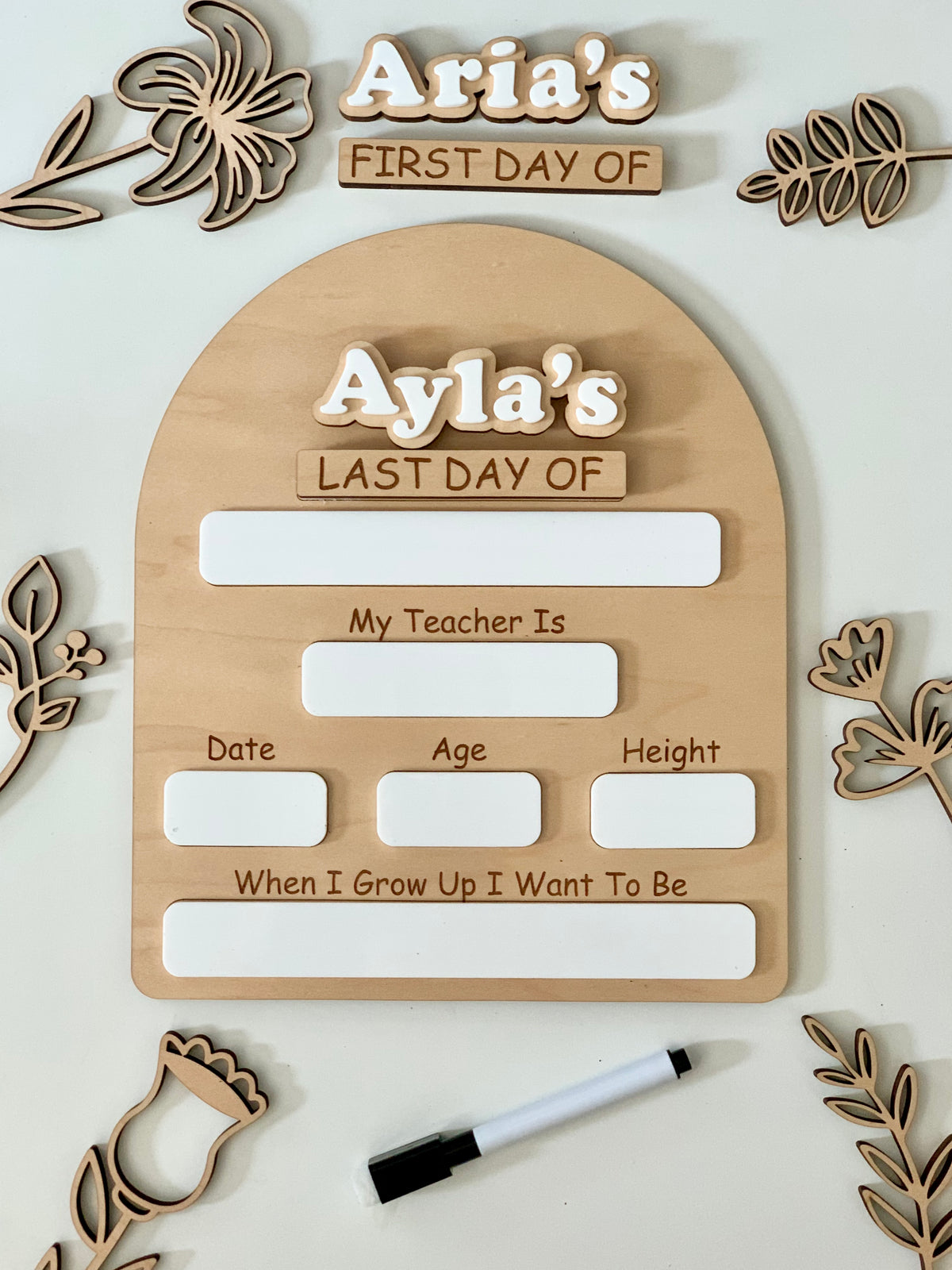 Wooden dry erase first and last day of school sign with white acrylic name pieces and black dry erase marker surrounded by wood flowers