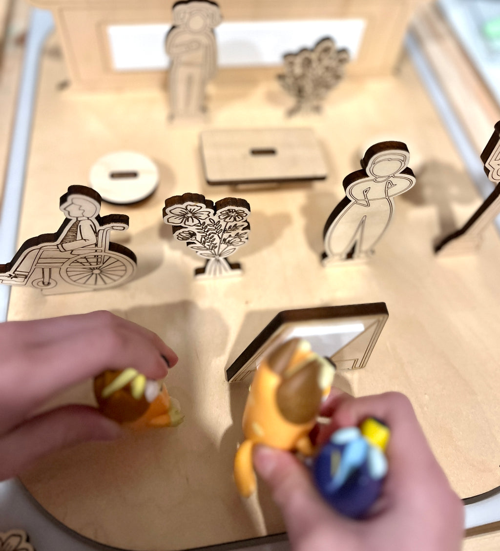 Wooden laser-cut figures including a person in a wheelchair, a standing woman, and floral designs on a light wood board