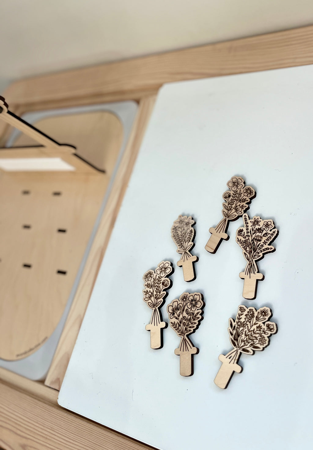 Six small wooden pieces shaped like flower bouquets with engraved floral details on a light-colored surface