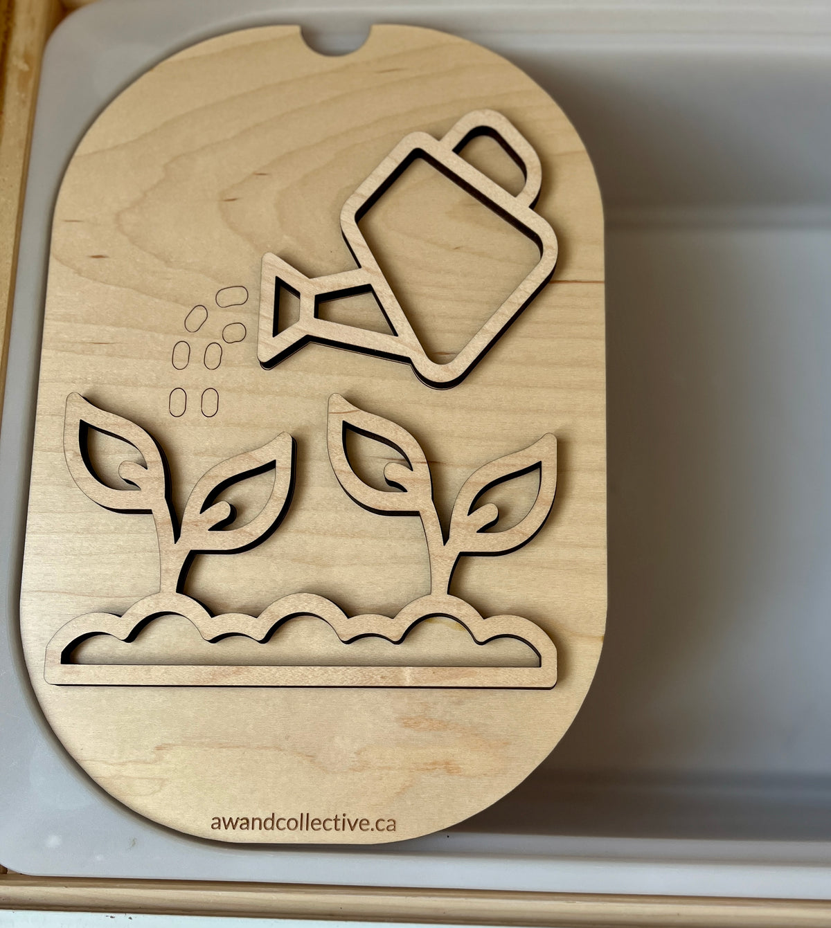 Light wood puzzle board with cutouts of a watering can pouring water over two seedlings in soil