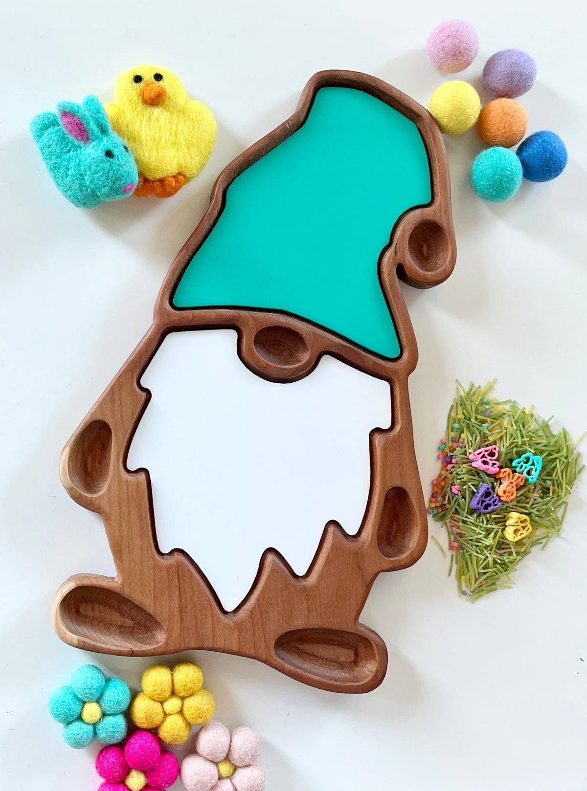 Wooden gnome-shaped sensory tray with turquoise hat and white beard surrounded by colorful pom-poms and felt toys