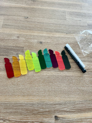 A row of colorful translucent candle-shaped pieces arranged on a wooden surface next to black and white dry erase markers, featuring Little Dry Erasables - Translucent Candles - Set of 5 or 10, handcrafted homeschool education resources.