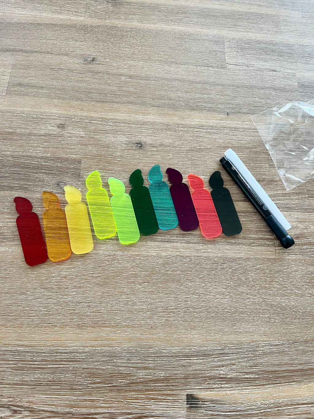 A row of colorful translucent candle-shaped pieces arranged on a wooden surface next to black and white dry erase markers, featuring Little Dry Erasables - Translucent Candles - Set of 5 or 10, handcrafted homeschool education resources.