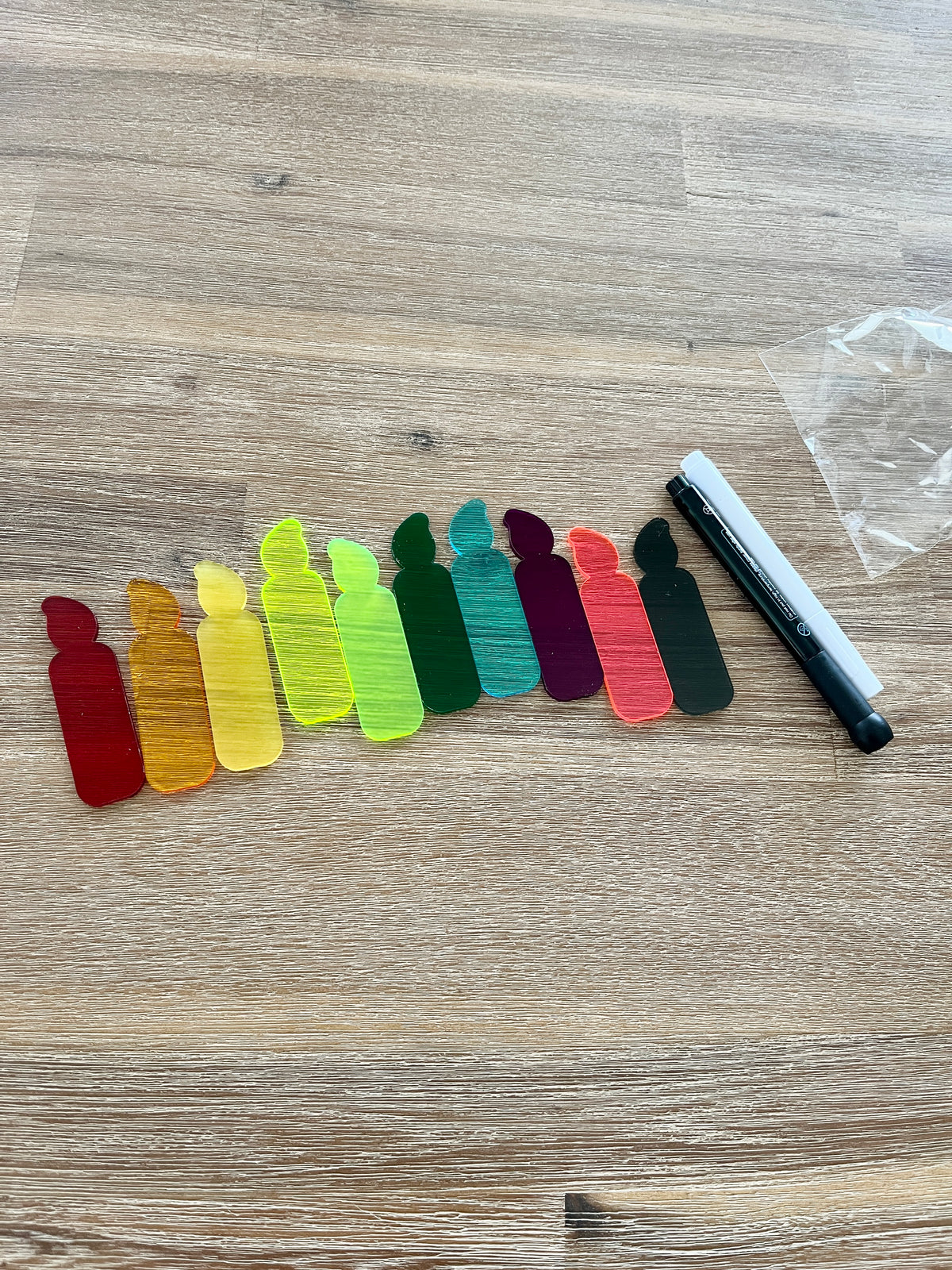 A row of colorful translucent candle-shaped pieces arranged on a wooden surface next to black and white dry erase markers, featuring Little Dry Erasables - Translucent Candles - Set of 5 or 10, handcrafted homeschool education resources.