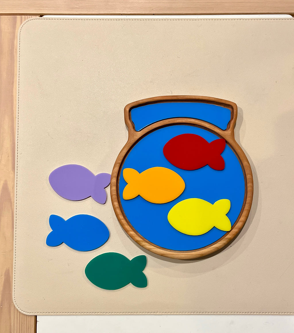 Wooden fish bowl sensory tray with colorful wooden fish pieces in red, yellow, orange, purple, blue, and green on beige surface