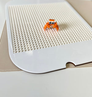 White acrylic Flisat table top insert with Lego studs and small orange buildable figurine on beige surface