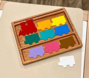 Wooden colorful train puzzle pieces in red, yellow, blue, green, teal, purple, pink, brown, and white on a light surface