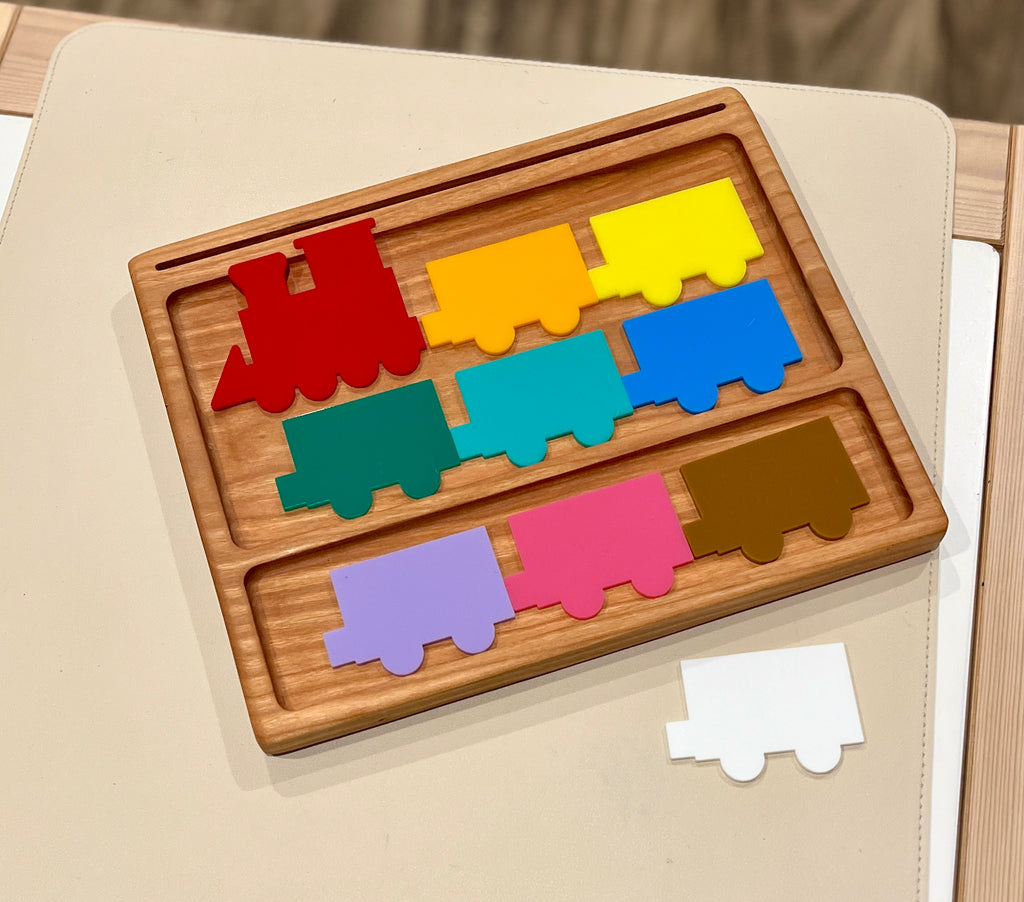 Wooden colorful train puzzle pieces in red, yellow, blue, green, teal, purple, pink, brown, and white on a light surface