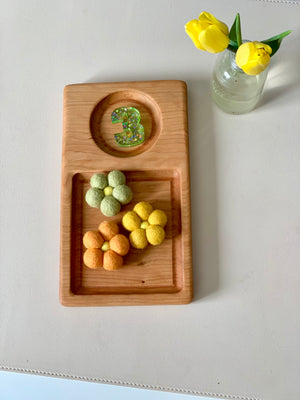 Wooden tray with glittery number three and three felt flowers in green, orange, and yellow next to a small jar with yellow tulips