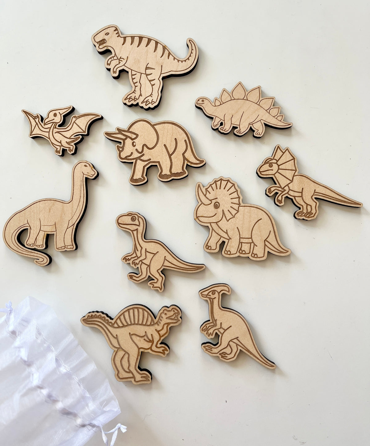 Ten wooden dinosaur figures including T-Rex, Triceratops, Stegosaurus, and Pterodactyl on a white surface