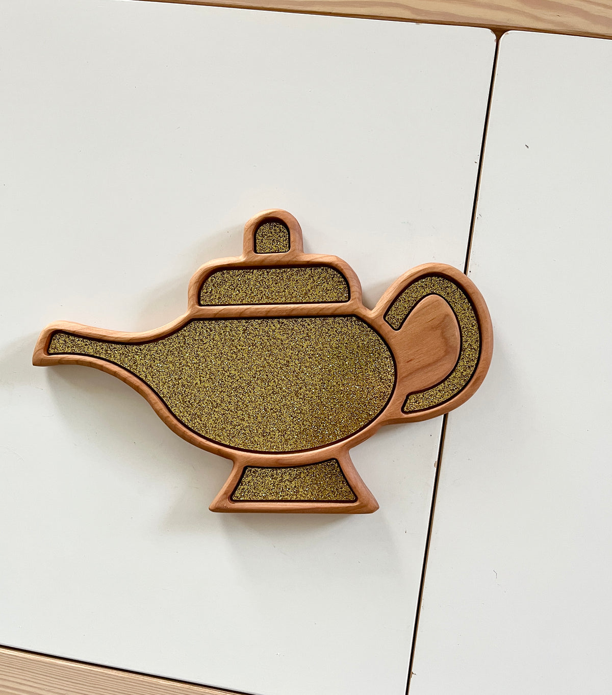 Wooden tray shaped like a genie lamp with textured gold interior and smooth wooden edges on white surface