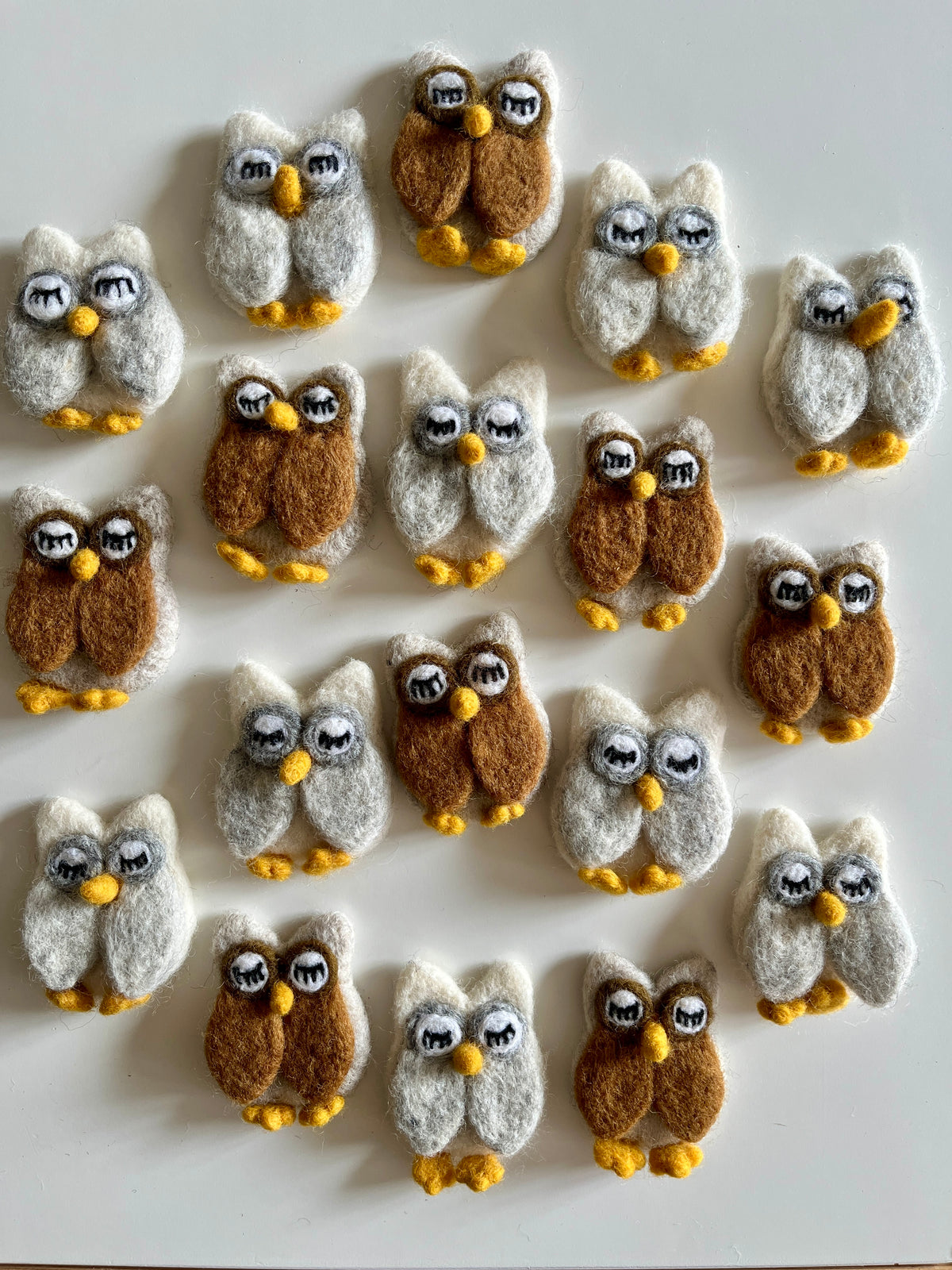 Collection of small handmade felt owl figures in white and brown shades arranged on a white surface