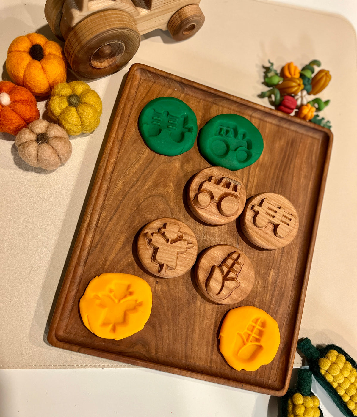 Wooden stamps and matching yellow and green playdough impressions on a wooden tray with felt pumpkins and toy truck nearby