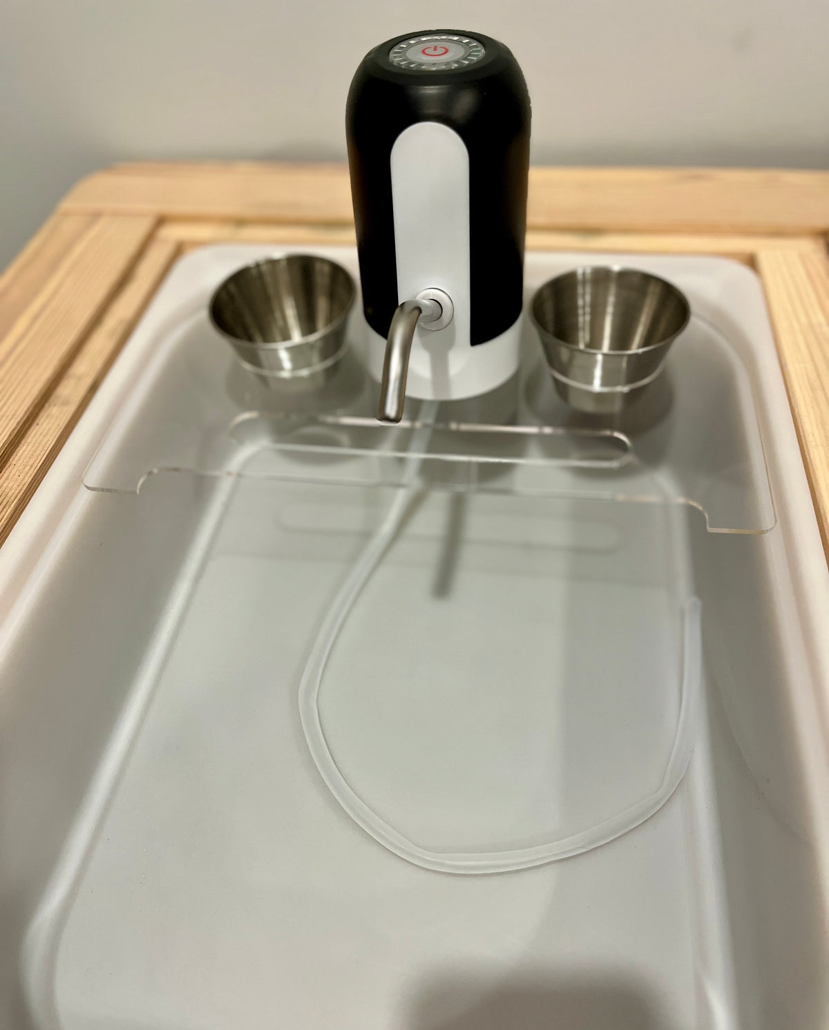 Black and white play kitchen faucet with silver metal cups and detachable white water pump on wooden surface