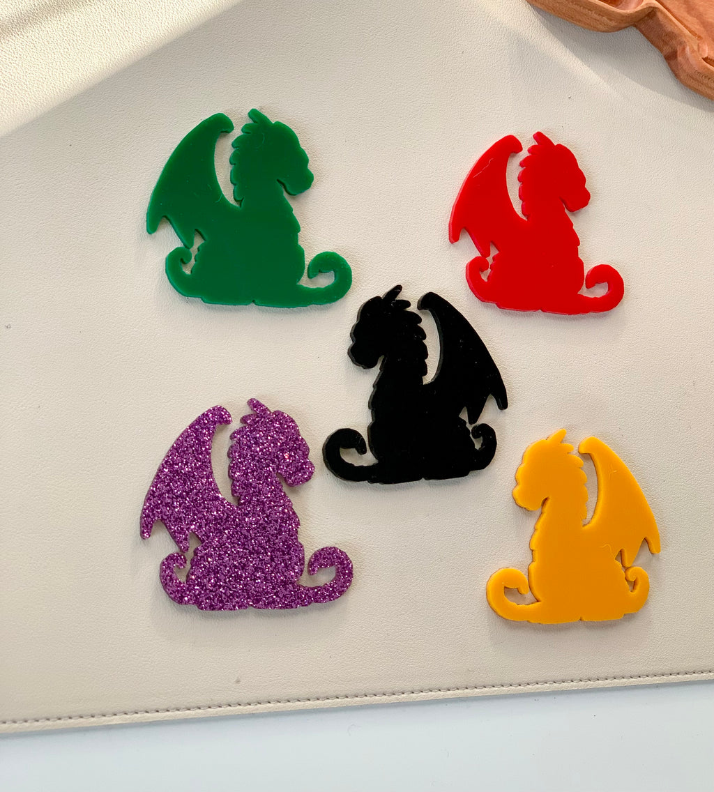 Five dragon-shaped plastic pieces in green, red, black, yellow, and purple glitter on white surface