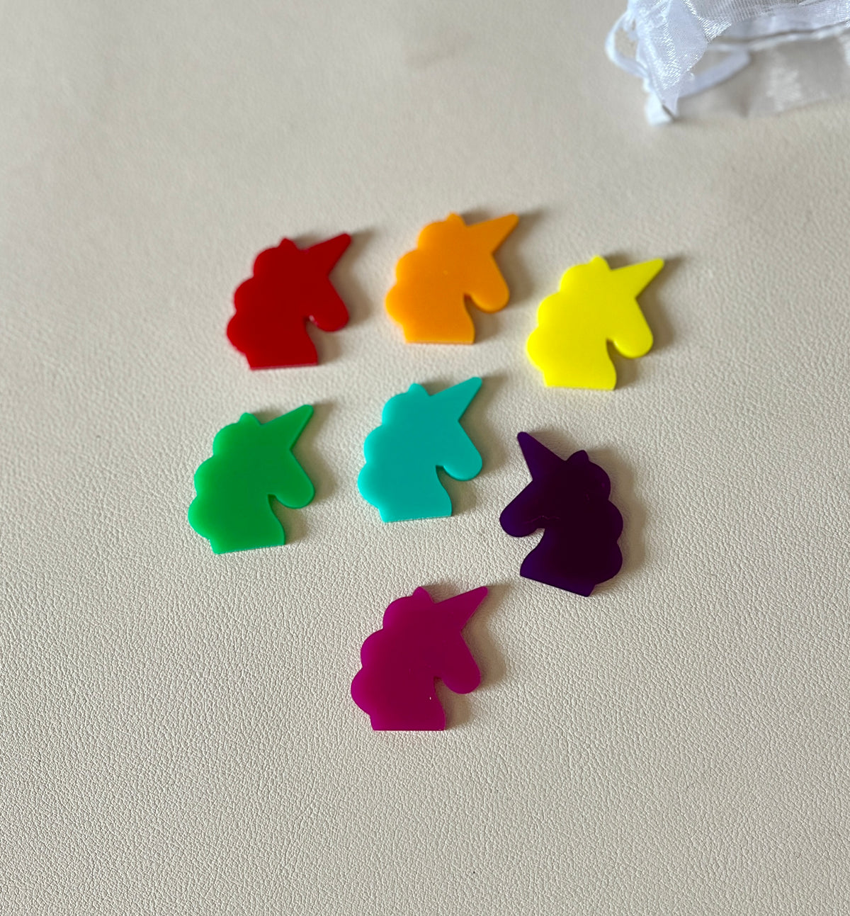 Seven colorful unicorn-shaped plastic pieces in red, orange, yellow, green, teal, purple, and pink on a beige surface