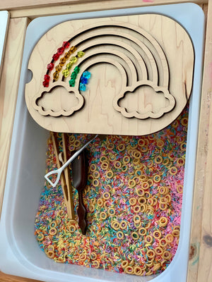 Wooden rainbow puzzle with colorful gems above a sensory bin filled with dyed rice and cereal rings with scooping tools