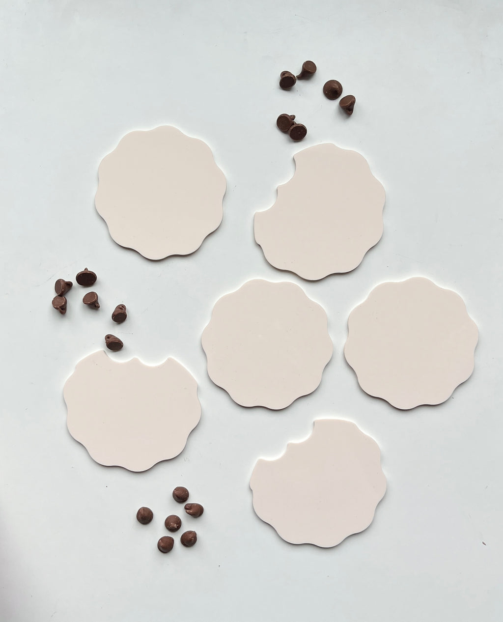 Six scalloped beige cookie cutouts with three bitten edges arranged with scattered chocolate chips on white surface