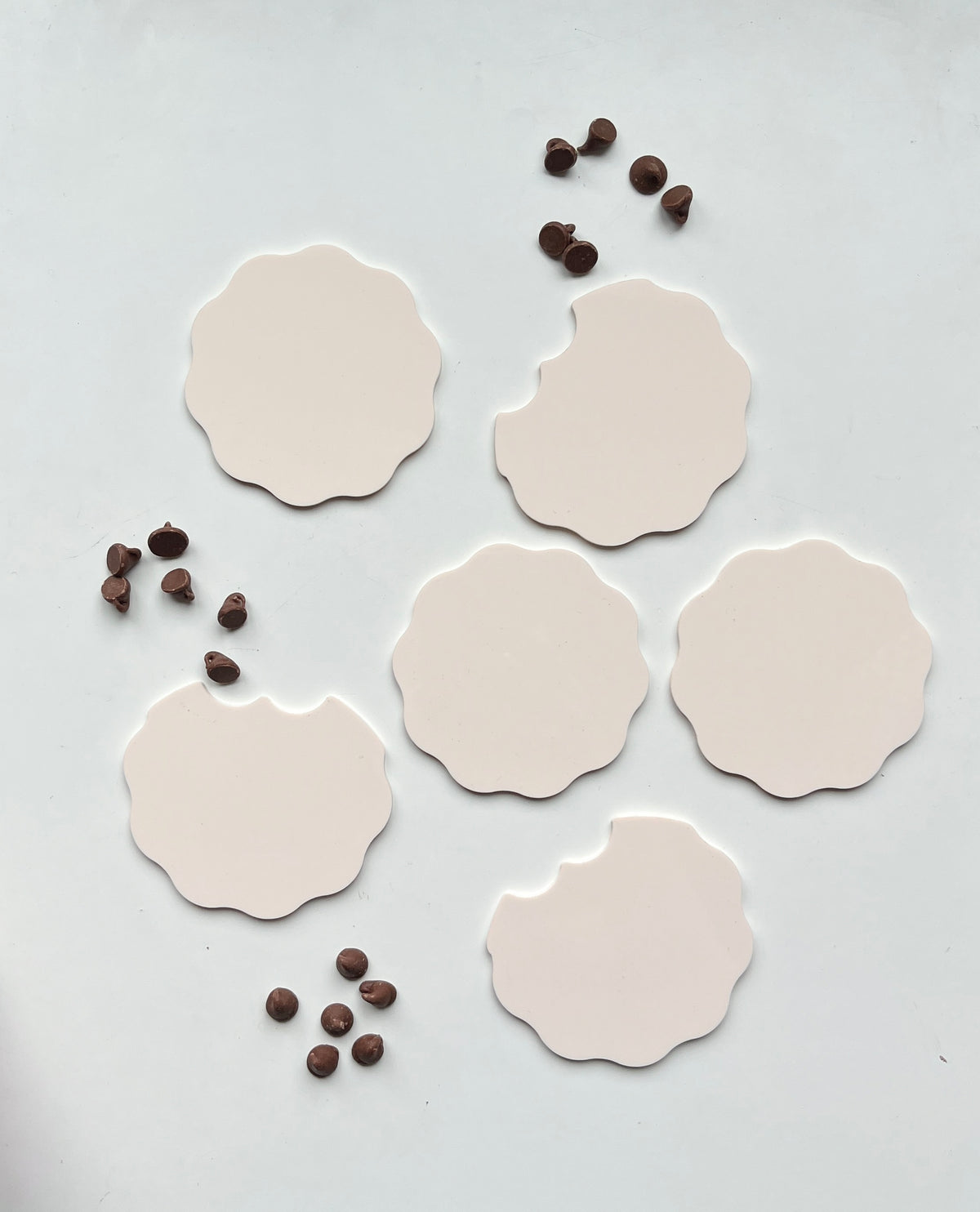 Six scalloped beige cookie cutouts with three bitten edges arranged with scattered chocolate chips on white surface