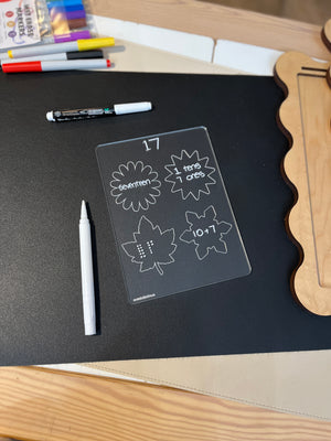 Clear learning board with the number 17 shown as word, tens and ones, dots, and equation on black surface