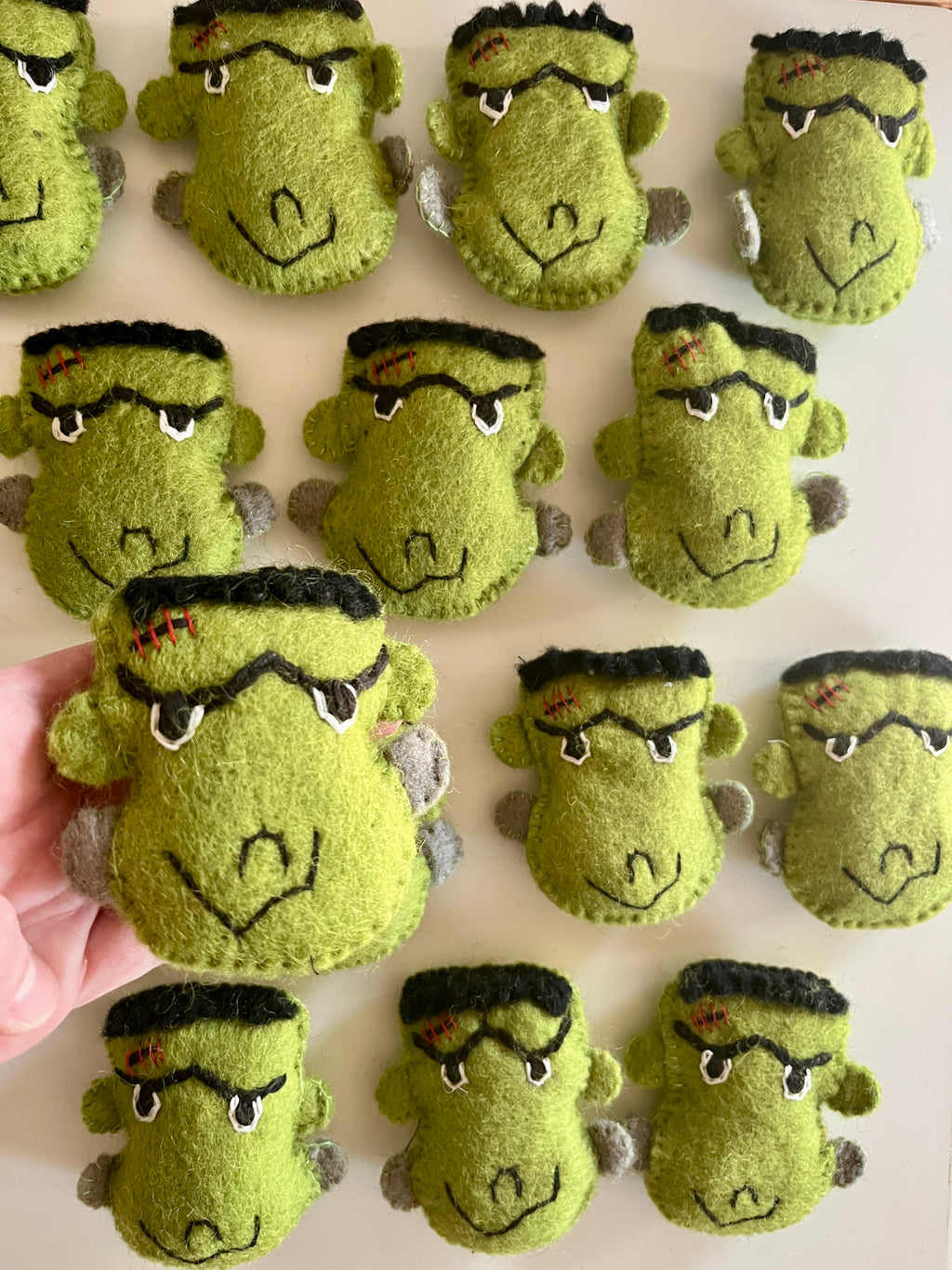 Collection of handmade green felt Frankenstein monster face plushies with black hair and stitched scar details on light background