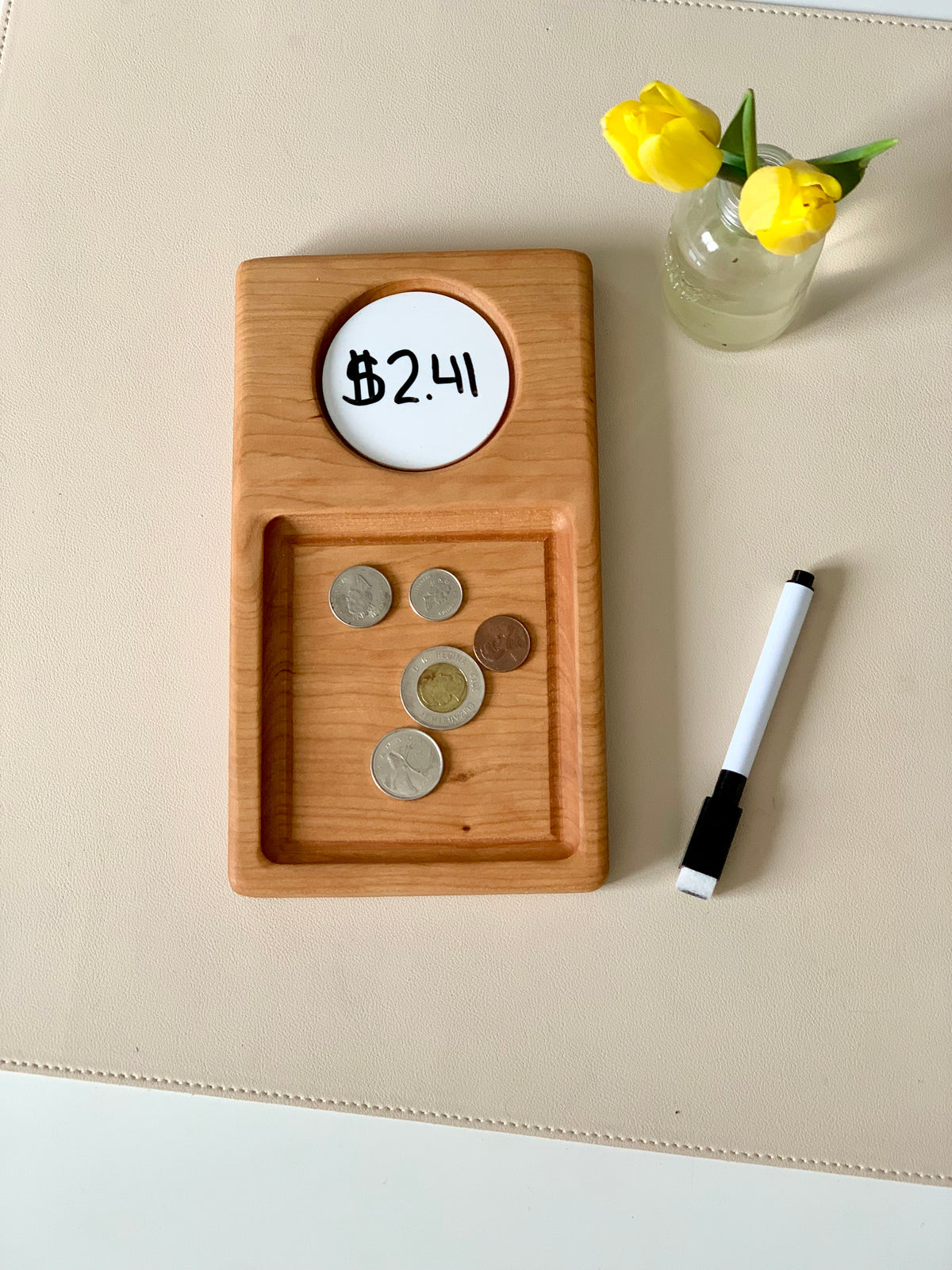 Wooden tray with coins in the lower compartment and a dry erase circle showing $2.41, marker and yellow tulips nearby