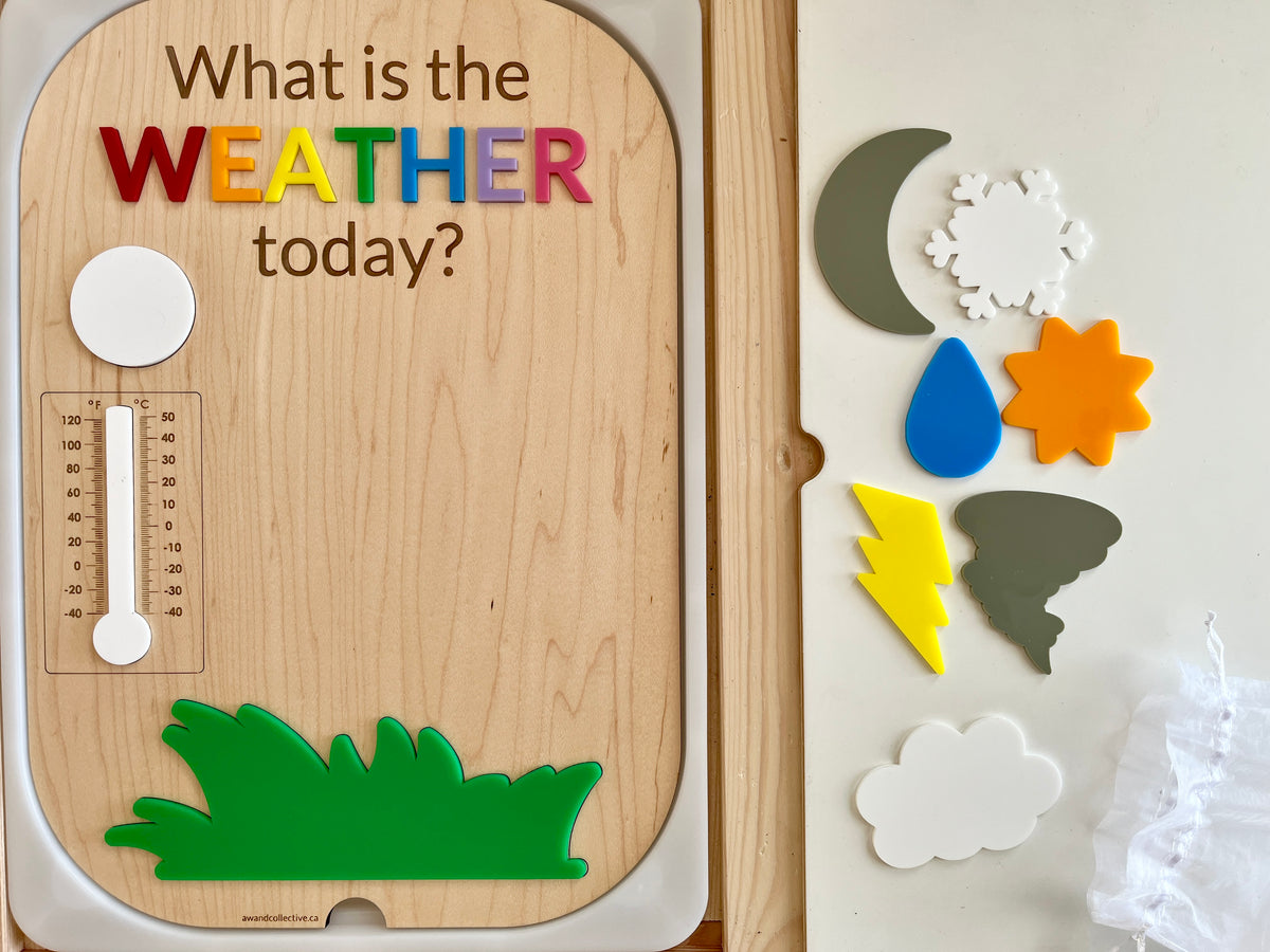 Wooden weather board with colorful magnetic letters spelling WEATHER and various weather symbol magnets including sun, cloud, and lightning bolt