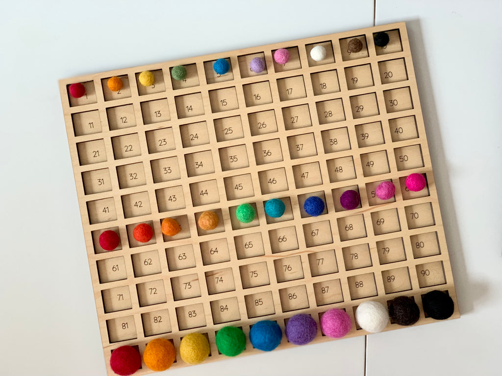 Wooden 100 frame sorting board with colorful felt balls in each numbered square on white surface