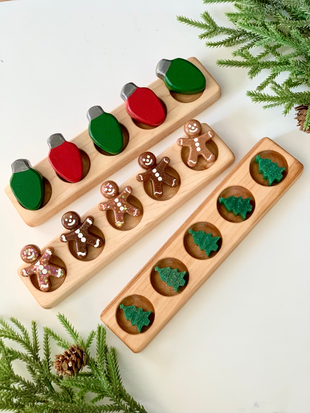 Three wooden five frame sensory trays with painted Christmas light bulbs, gingerbread men, and green tree shapes on white table