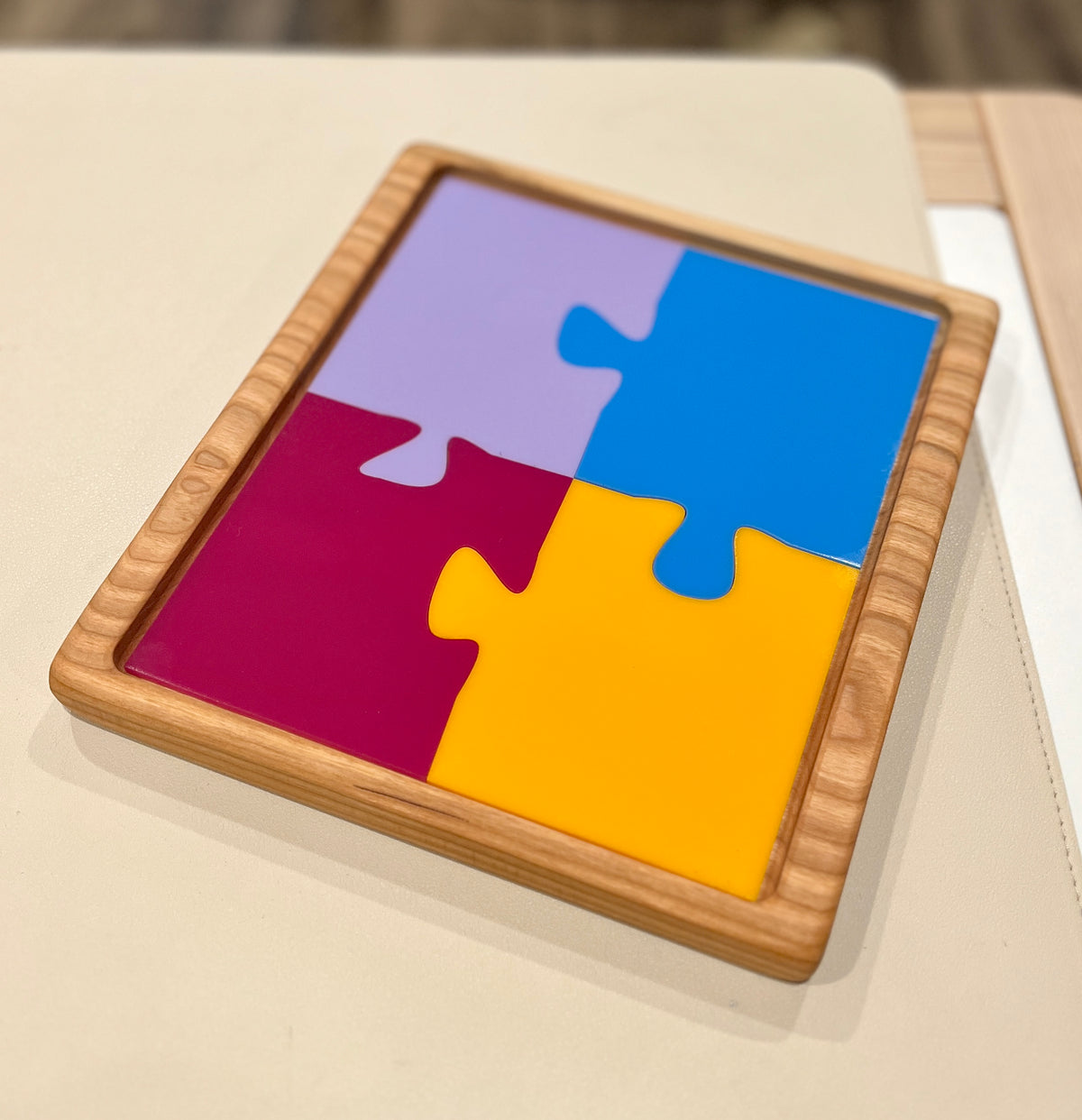 Wooden tray holding four large colorful interlocking puzzle pieces in purple, blue, red, and yellow on a light surface