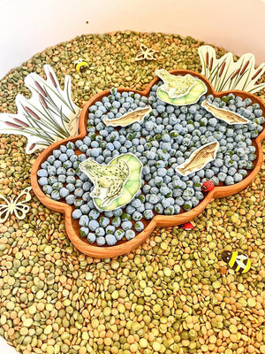 Cloud shaped wooden sensory tray filled with blue beads and nature-themed paper cutouts on a lentil background