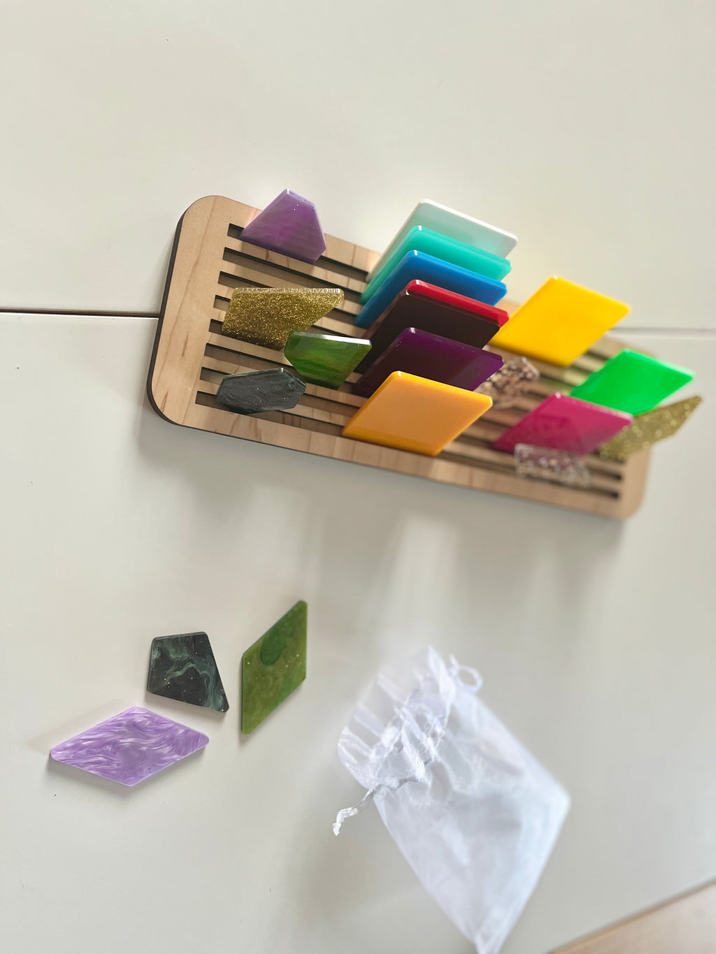 Wooden magnetic rack holding colorful acrylic geometric shapes with several shapes and a white pouch on white surface below