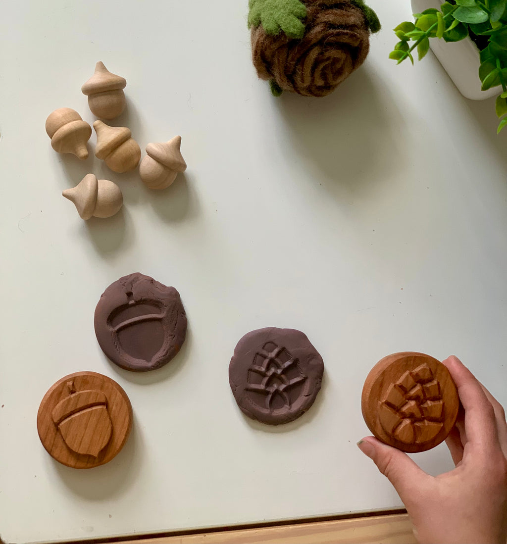 Light wooden acorn figurines with carved wooden stamps and matching impressions on clay on white surface