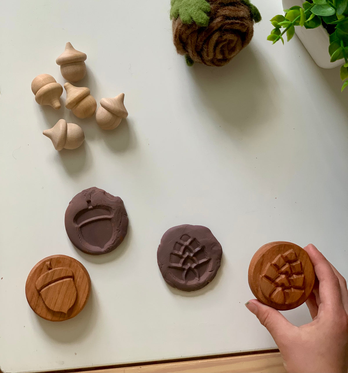 Light wooden acorn figurines with carved wooden stamps and matching impressions on clay on white surface