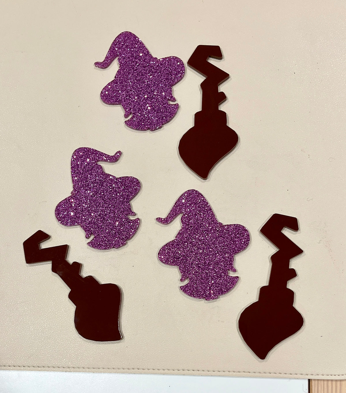 Three purple glitter witch head shapes and three dark red jagged key cutouts on a light surface