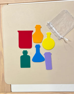 Set of six colorful dry erasable beaker and potion bottle shapes with sheer storage bag on beige surface