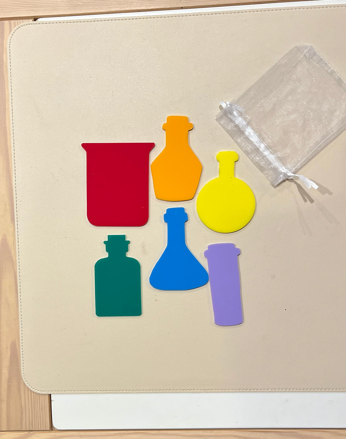 Set of six colorful dry erasable beaker and potion bottle shapes with sheer storage bag on beige surface