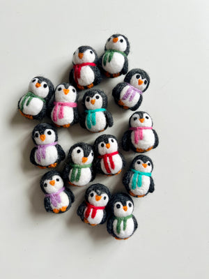 Collection of small handmade felt penguins wearing scarves in various colors arranged on white surface