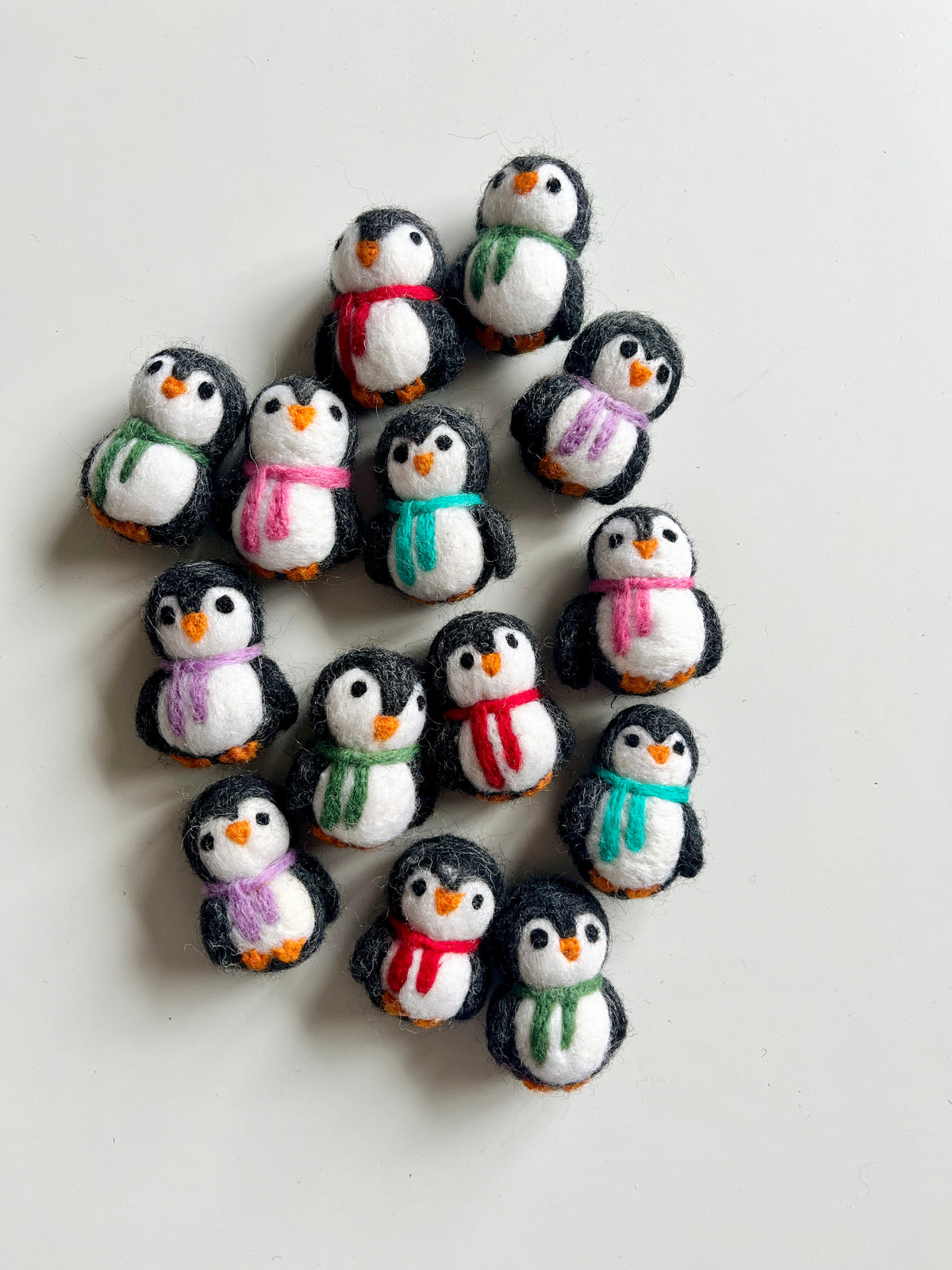 Collection of small handmade felt penguins wearing scarves in various colors arranged on white surface
