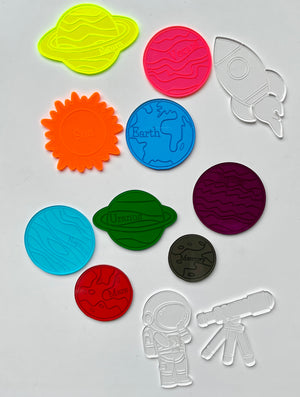 Colorful plastic cookie cutters shaped like planets, the sun, an astronaut, a rocket, and a telescope on white background